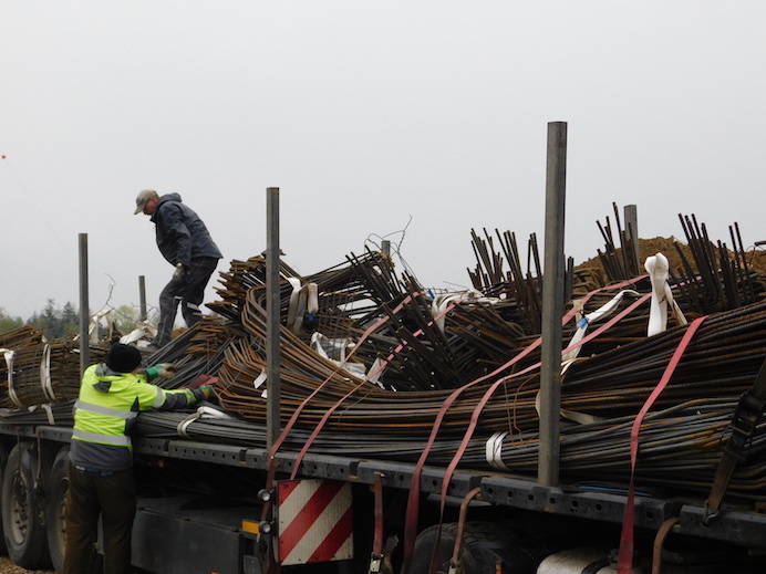 heavy dark iron bars on a truck, bad weather, a worker with neon yellow raincoat is unloading