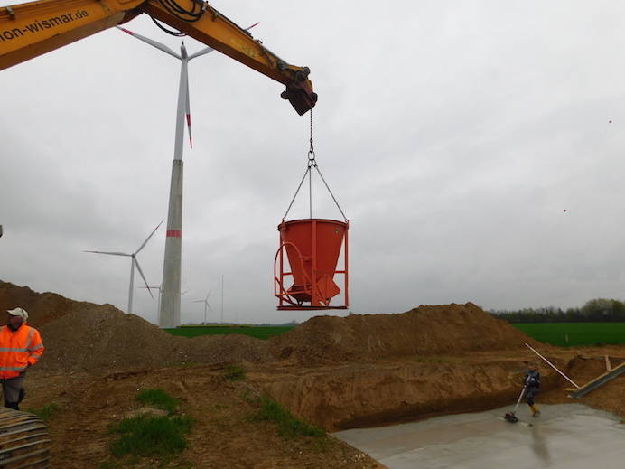 crane reaches bucket with concrete to the workers in the pit