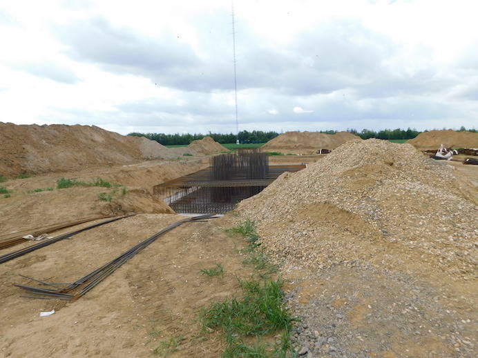 Behind a mound rises the steel framework of a pedestal. You can look from the side into the interior.